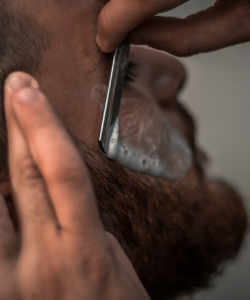 Barbeiro fazendo a barba de um homem com navalha